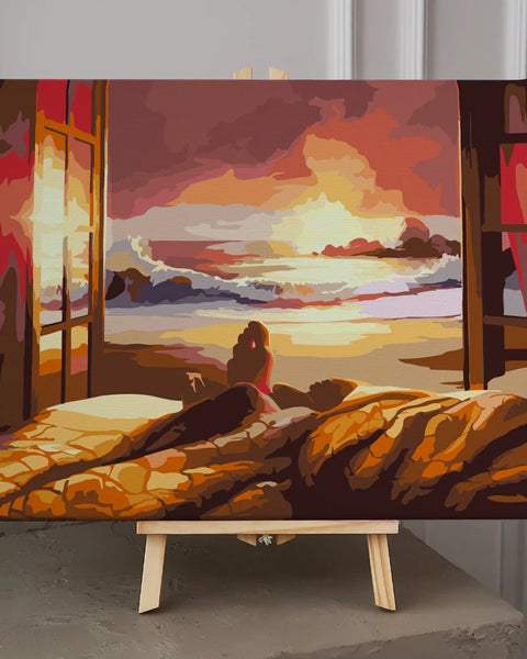 Person watching sunset over ocean from cozy bed near window