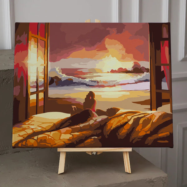 Person watching sunset over ocean from cozy bed near window