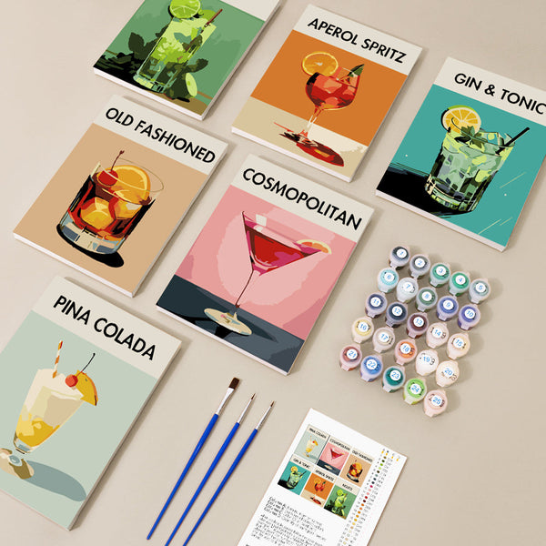 "Contents of the Sip Society cocktail canvas set of 6 paint by numbers by Artspark displayed on a flat surface. Includes 6 mini canvases featuring Aperol Spritz, Cosmopolitan, Pina Colada, Mojito, Gin & Tonic, and Old Fashioned. The set also includes numbered paint pots, three paint brushes, and a reference guide with thumbnail images of all canvases.