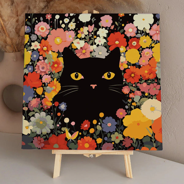 Black cat with yellow eyes surrounded by colorful blooming flowers