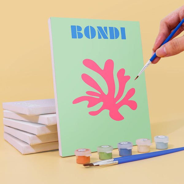 Coastal Dreams Paint by Numbers Kit by Artspark showing the painting process of the Bondi canvas with paint pots, brush, and stacked canvases.