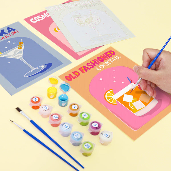 Cocktail Cuties Paint by Numbers Kit by Artspark showing painting progress on the Old Fashioned cocktail canvas, surrounded by paint pots, brushes, and additional unpainted cocktail-themed canvases.