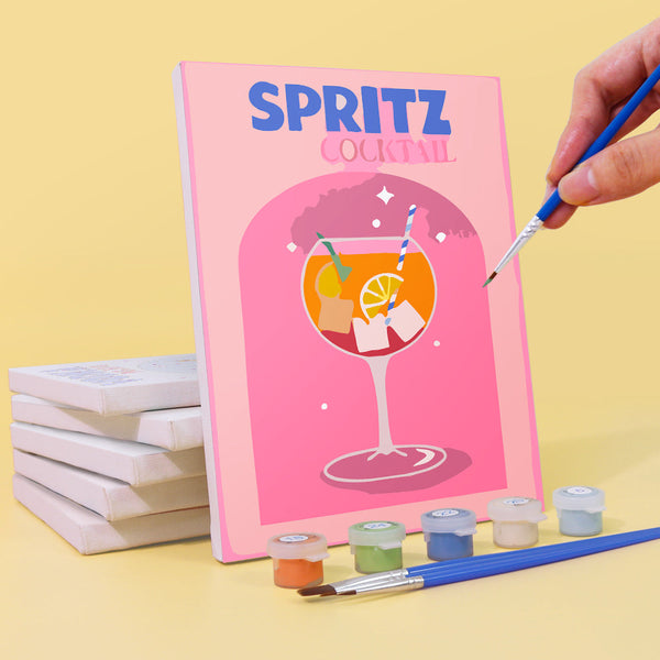 Cocktail Cuties Paint by Numbers Kit by Artspark showing the painting process of the Spritz canvas with paint pots, brush, and stacked canvases.