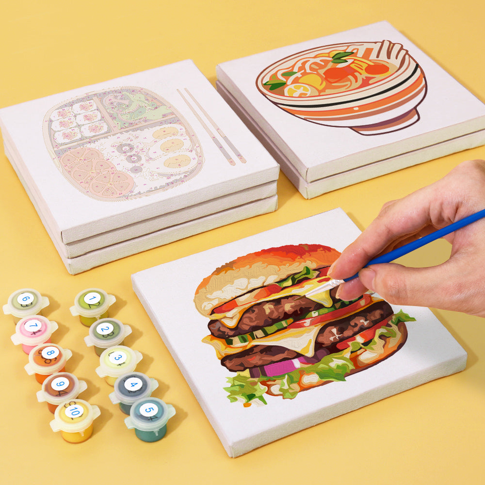 Painting progress of a burger canvas from the Flavors Around paint by numbers set, with paint pots and brush on display.