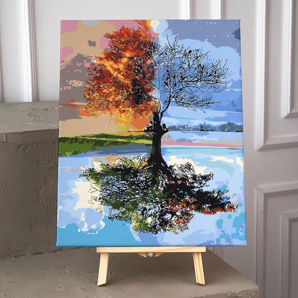 A tree depicting both summer and winter with a reflective lake
