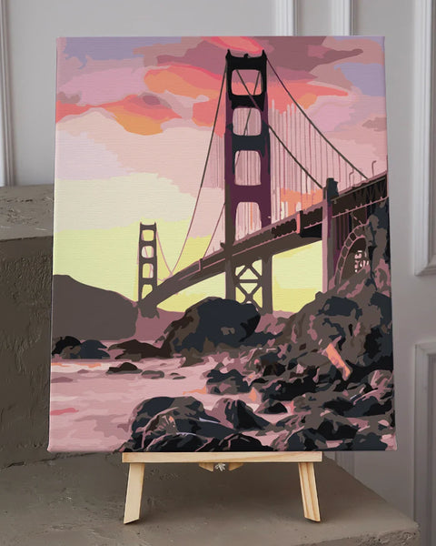 Golden Gate Bridge painting with sunset sky and rocky shoreline