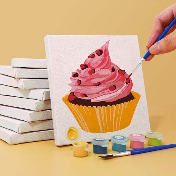 Sugar & Whimsy Paint by Numbers Kit by Artspark showing the painting process of a pink cupcake canvas with paint pots and stacked canvases.