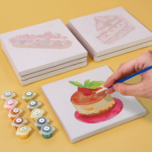 Sugar & Whimsy Paint by Numbers Kit by Artspark showing the painting process of a cheesecake canvas with paint pots and stacked canvases.